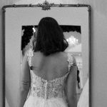 Back view of a bride in a lace wedding gown gazing into a mirror, highlighting a milestone in her wedding planning timeline