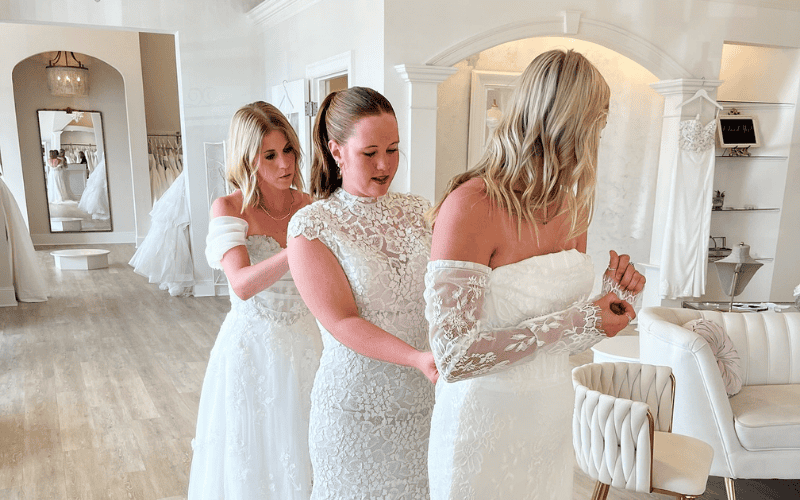three brides helping each other fit on a dress