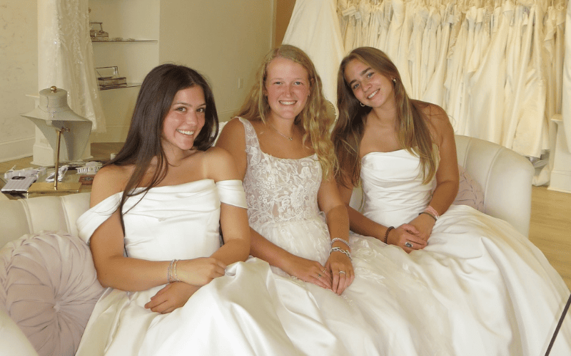 three women wearing a wedding dress sitting in the couch of ashley grace bridal